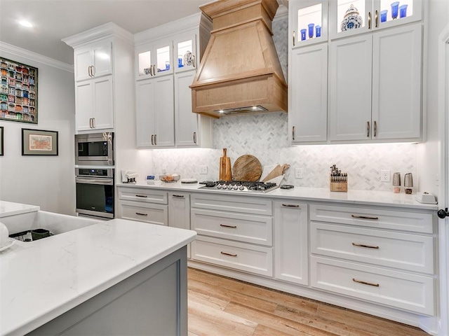 kitchen featuring crown molding, stainless steel appliances, decorative backsplash, white cabinets, and premium range hood