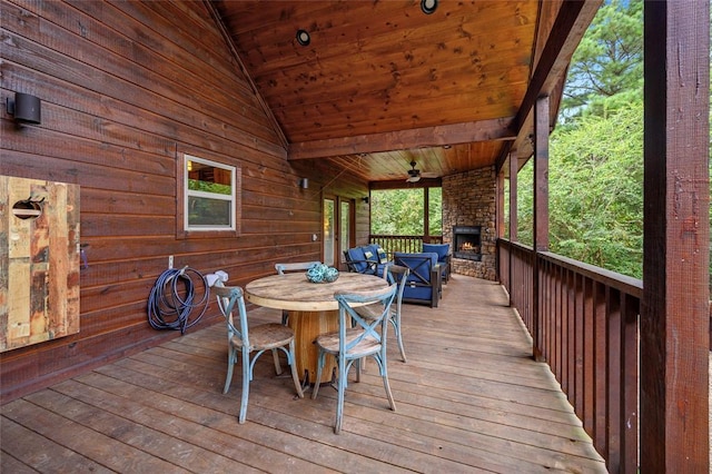 deck with an outdoor stone fireplace, outdoor dining space, and a ceiling fan