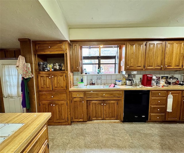 kitchen featuring a sink, backsplash, black dishwasher, and brown cabinetry