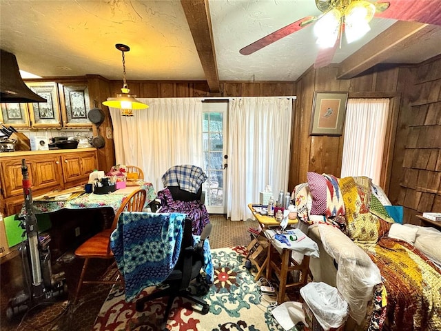 dining room with beamed ceiling, wooden walls, ceiling fan, and a textured ceiling