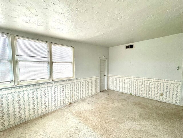 carpeted spare room with a wainscoted wall, a textured ceiling, and visible vents