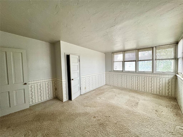 unfurnished room featuring a wainscoted wall, carpet flooring, wallpapered walls, and a textured ceiling