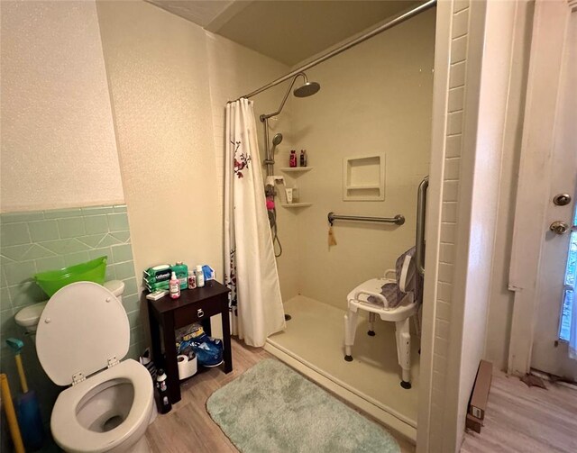 bathroom featuring toilet, a shower stall, wood finished floors, and tile walls