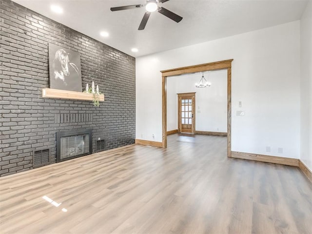 unfurnished living room featuring a brick fireplace, baseboards, visible vents, and wood finished floors