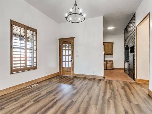 unfurnished dining area with dark wood-style flooring, visible vents, baseboards, and an inviting chandelier