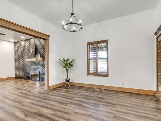 unfurnished living room featuring a fireplace, wood finished floors, an inviting chandelier, and baseboards