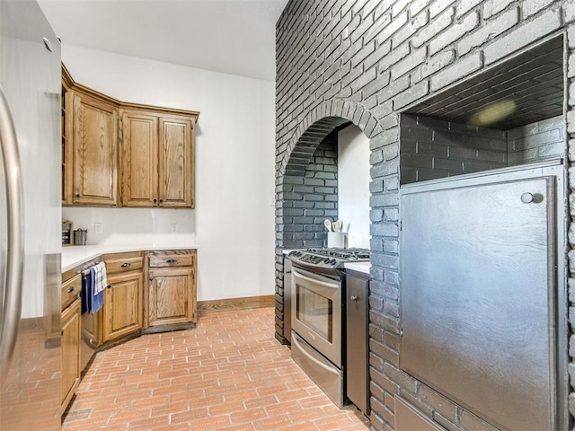 kitchen featuring stainless steel appliances, brown cabinets, light countertops, and baseboards