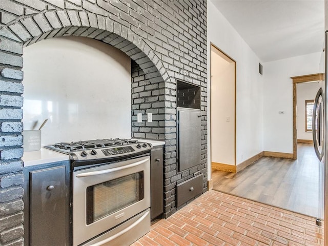 kitchen featuring brick floor, stainless steel appliances, light countertops, visible vents, and baseboards