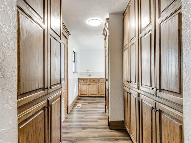 hallway featuring a textured ceiling, a textured wall, light wood-style flooring, and baseboards