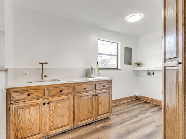 kitchen with light countertops, light wood-style floors, a sink, electric panel, and baseboards