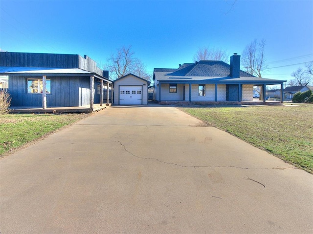 view of front of home featuring a chimney, a front lawn, concrete driveway, and an outbuilding