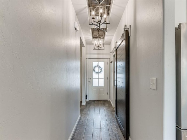 doorway featuring a chandelier, wood finished floors, baseboards, and a barn door