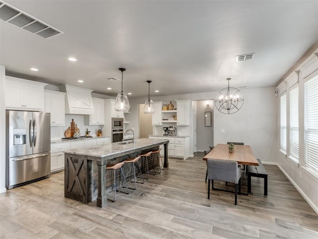 kitchen with open shelves, a kitchen island with sink, visible vents, and stainless steel appliances