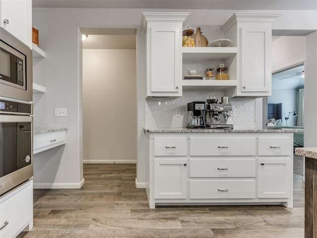 kitchen featuring decorative backsplash, stainless steel microwave, light stone countertops, light wood-style floors, and open shelves