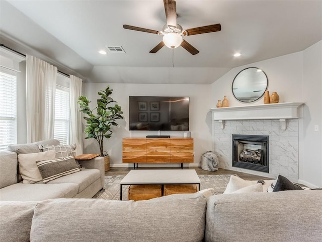 living room featuring ceiling fan, a fireplace, visible vents, baseboards, and vaulted ceiling