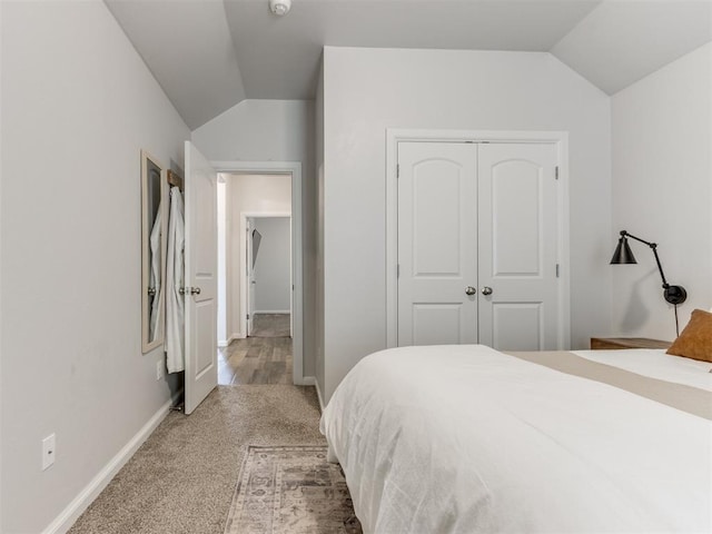 bedroom with lofted ceiling, a closet, light colored carpet, and baseboards