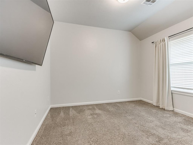 carpeted empty room with baseboards, visible vents, and vaulted ceiling