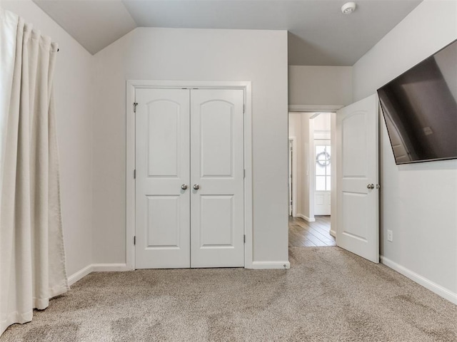 unfurnished bedroom with lofted ceiling, a closet, carpet flooring, and baseboards