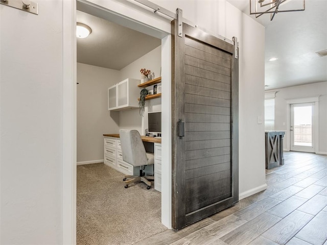 office area featuring light carpet, built in desk, baseboards, and a barn door