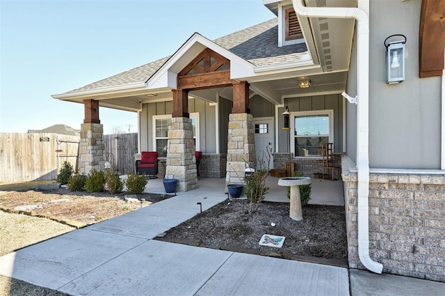 property entrance featuring covered porch, a shingled roof, fence, and board and batten siding