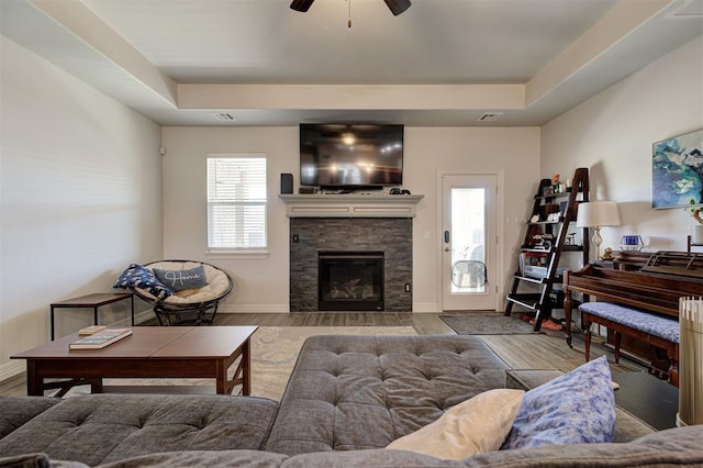 living room featuring a stone fireplace, wood finished floors, a raised ceiling, and visible vents