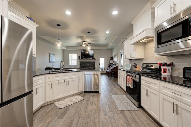 kitchen featuring light wood finished floors, decorative backsplash, appliances with stainless steel finishes, open floor plan, and a sink