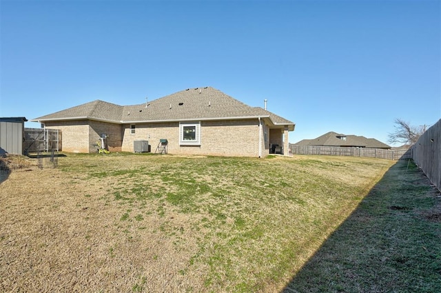 back of property with central AC, brick siding, a lawn, and a fenced backyard