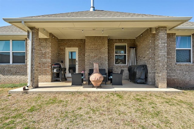 back of property with a patio, brick siding, a lawn, and roof with shingles