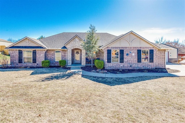 view of front of property featuring a shingled roof, a front yard, and brick siding