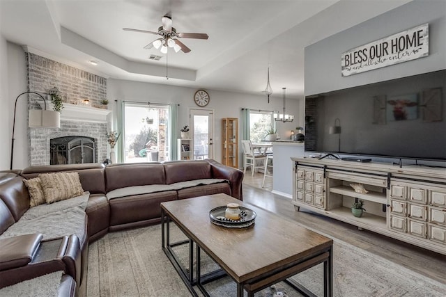 living area featuring ceiling fan, wood finished floors, visible vents, a brick fireplace, and a raised ceiling