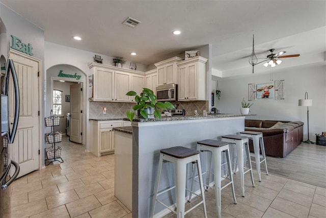 kitchen featuring visible vents, arched walkways, stainless steel microwave, open floor plan, and a kitchen breakfast bar