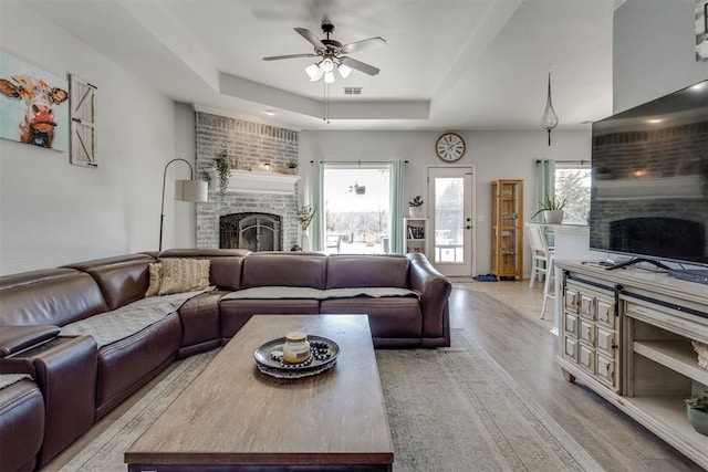 living room with a ceiling fan, light wood-type flooring, a raised ceiling, and a fireplace