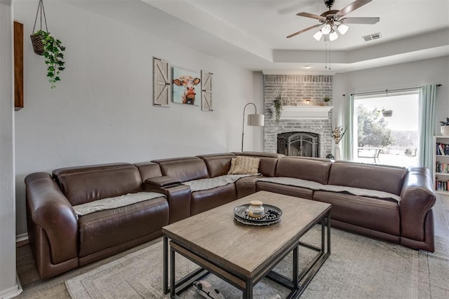 living room with a fireplace, visible vents, a raised ceiling, and a ceiling fan