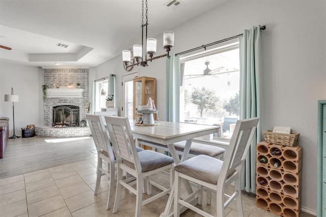 dining space with light tile patterned flooring, visible vents, a raised ceiling, and ceiling fan with notable chandelier