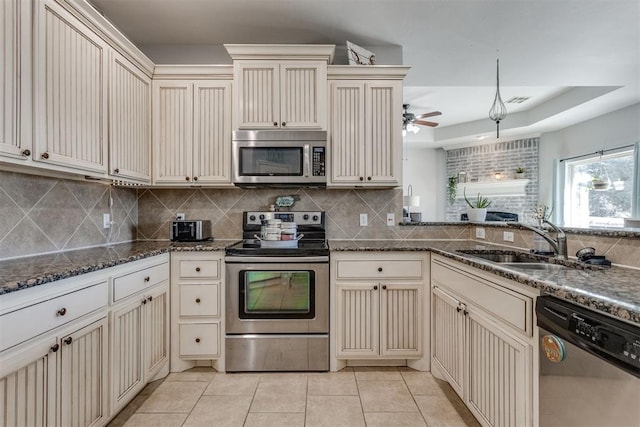 kitchen with stainless steel appliances, tasteful backsplash, cream cabinets, light tile patterned flooring, and a sink