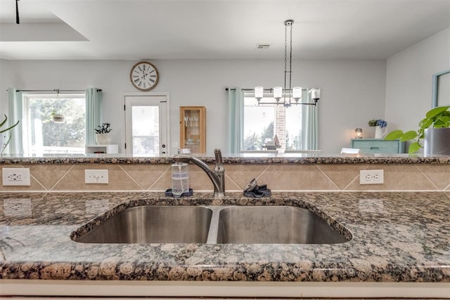 kitchen with dark stone counters, pendant lighting, visible vents, and a sink