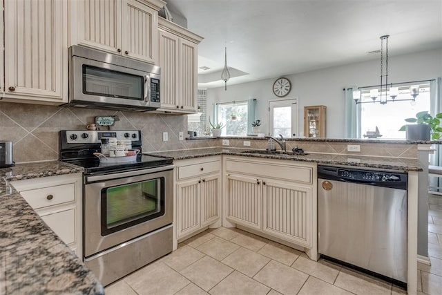 kitchen featuring decorative backsplash, appliances with stainless steel finishes, dark stone countertops, cream cabinets, and a sink