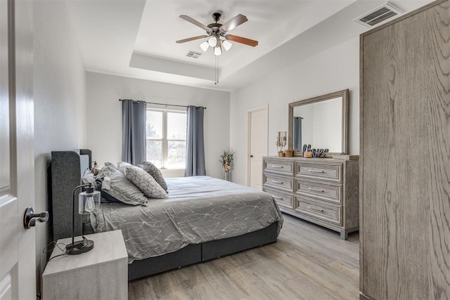 bedroom featuring light wood-type flooring, visible vents, a tray ceiling, and a ceiling fan