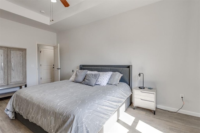 bedroom with a raised ceiling, ceiling fan, baseboards, and wood finished floors