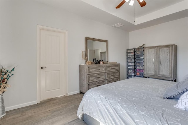 bedroom featuring light wood finished floors, a raised ceiling, visible vents, ceiling fan, and baseboards