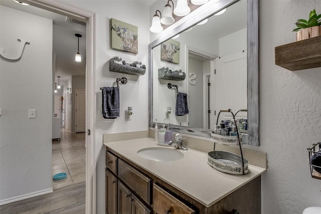 bathroom with a textured wall, wood finished floors, vanity, visible vents, and baseboards