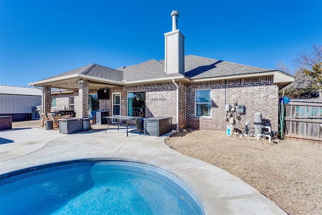 back of property with brick siding, fence, roof with shingles, a swimming pool, and a patio area