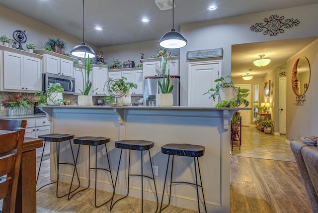 kitchen with hanging light fixtures, light wood-style flooring, appliances with stainless steel finishes, white cabinetry, and a kitchen breakfast bar