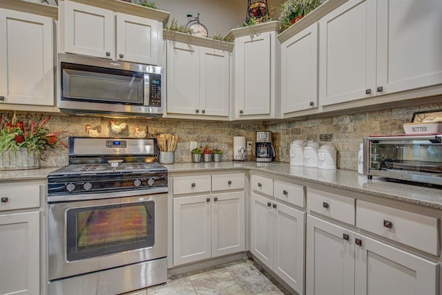 kitchen featuring light stone countertops, a toaster, appliances with stainless steel finishes, and decorative backsplash