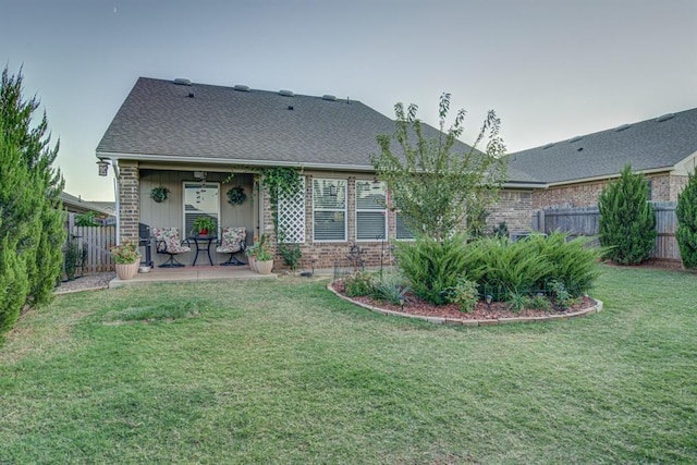 rear view of property featuring a yard, brick siding, a shingled roof, and fence