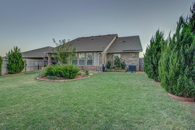 rear view of house with central air condition unit, brick siding, fence, and a yard