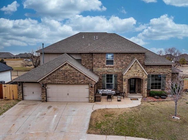 traditional-style house featuring an attached garage, brick siding, outdoor lounge area, fence, and roof with shingles