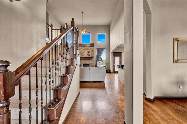 foyer entrance featuring arched walkways, a fireplace, wood finished floors, a towering ceiling, and baseboards