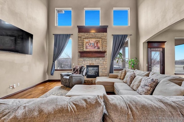 living area featuring a towering ceiling, a stone fireplace, wood finished floors, and a wealth of natural light