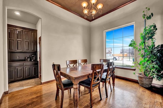 dining room with a chandelier, arched walkways, light wood-style flooring, baseboards, and crown molding